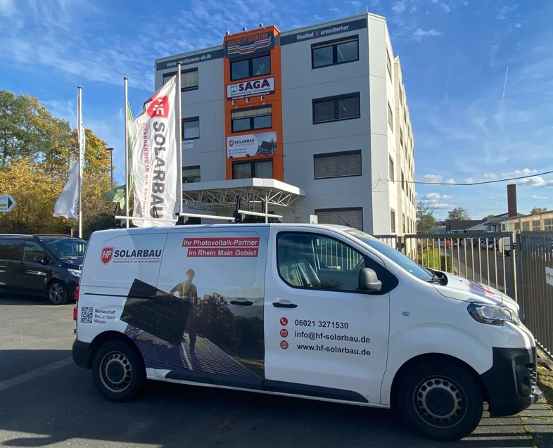 Ein weißer HF Solarbau Servicewagen mit Firmenlogo und der Aufschrift "Ihr Photovoltaik-Partner" parkt vor dem modernen Bürogebäude in Mainaschaff bei Aschaffenburg.