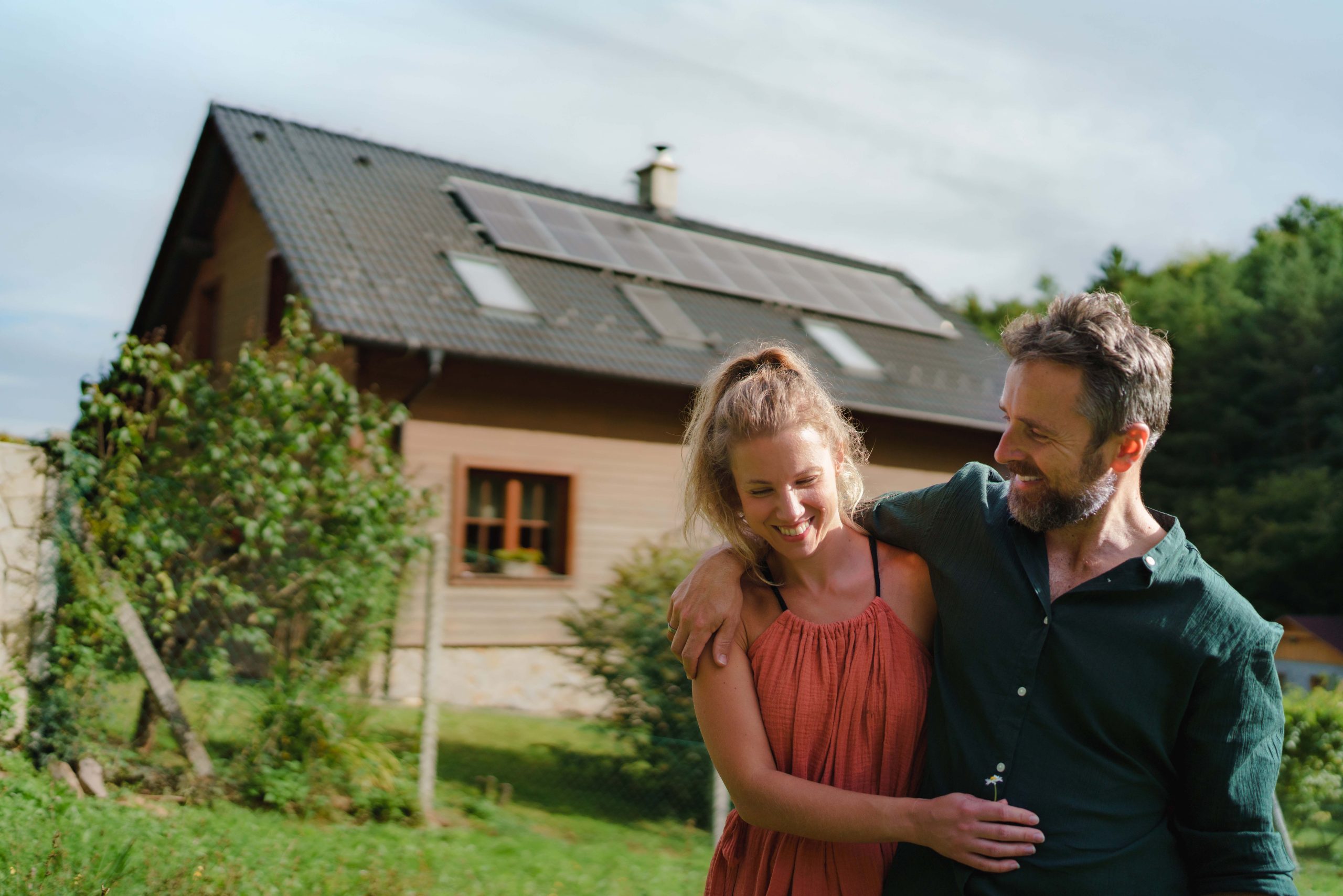 Ein glückliches Paar spaziert durch einen grünen Garten vor einem Einfamilienhaus mit einer installierten Photovoltaik Anlage in Aschaffenburg.