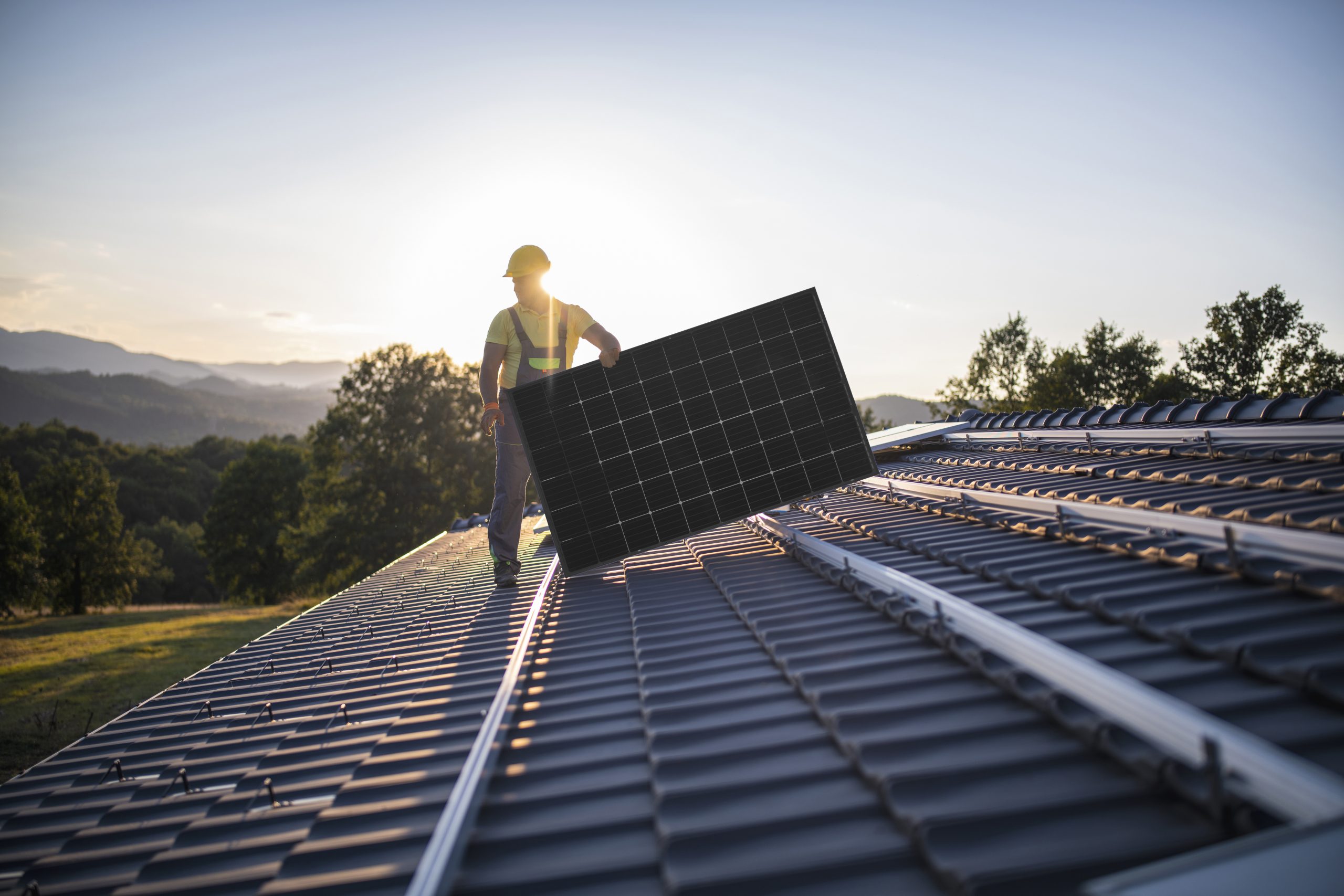 Solarmontage Photovoltaik Installation Ein qualifizierter Solarmonteur trägt ein Photovoltaik-Modul auf einem Hausdach.